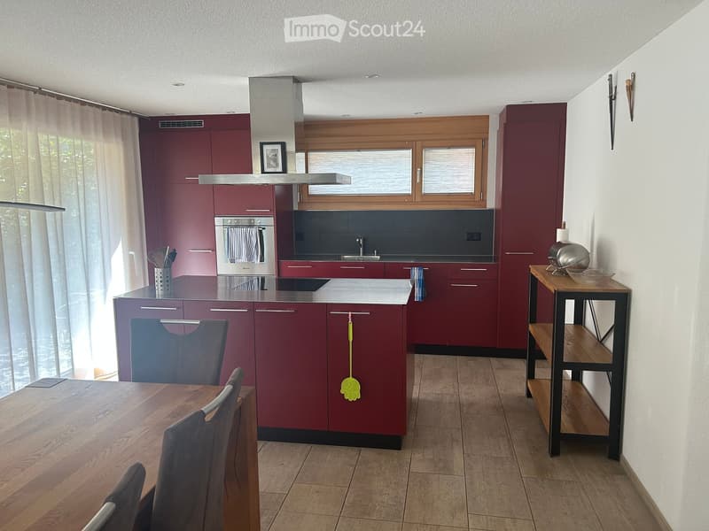 Modern kitchen with red cabinets, island, dining table, and various appliances.