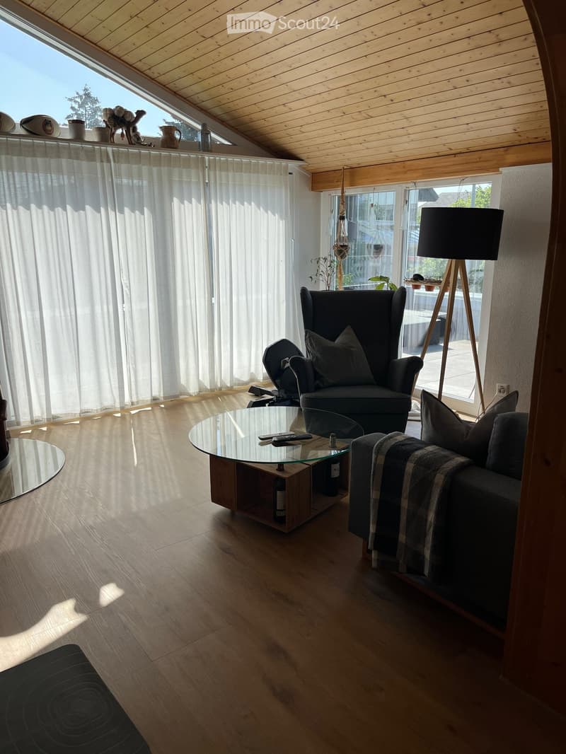 Modern living room with wooden floors, large windows, a sofa, armchair, coffee table, and floor lamp.