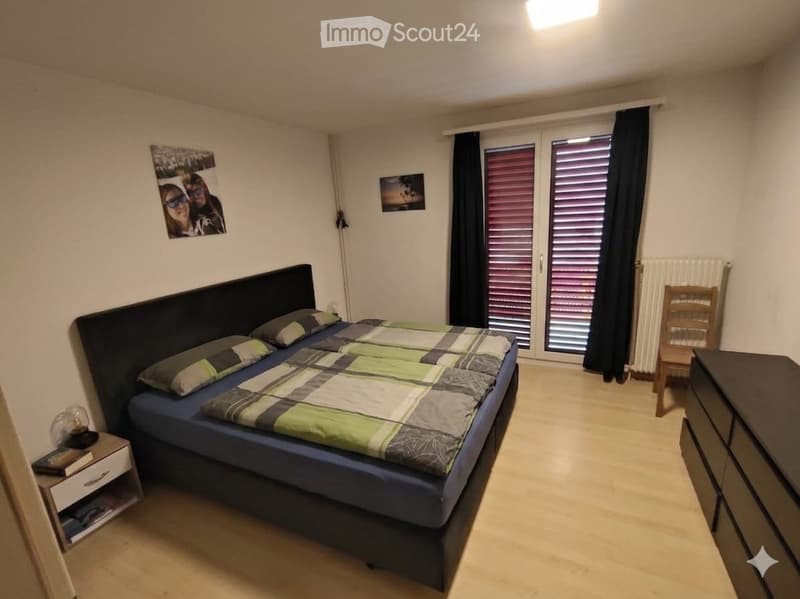 Cozy bedroom with a double bed, nightstand, chair, dresser, and picture frames on the walls.