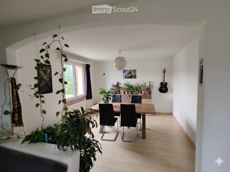 Bright dining area with wooden floor, large window, dining table with four chairs, potted plants, and a hanging lamp.