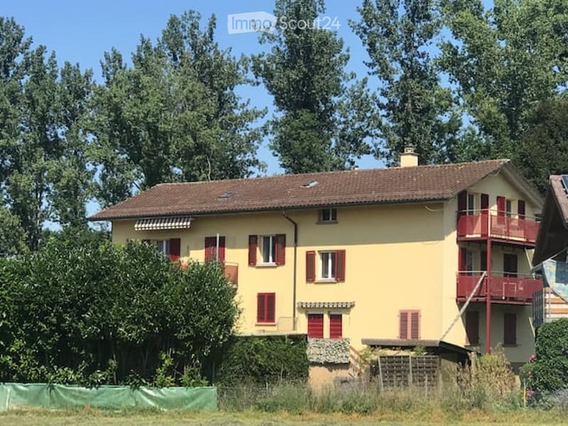 Two-story yellow house with red shutters, brown tiled roof, and a small balcony on the upper floor.
