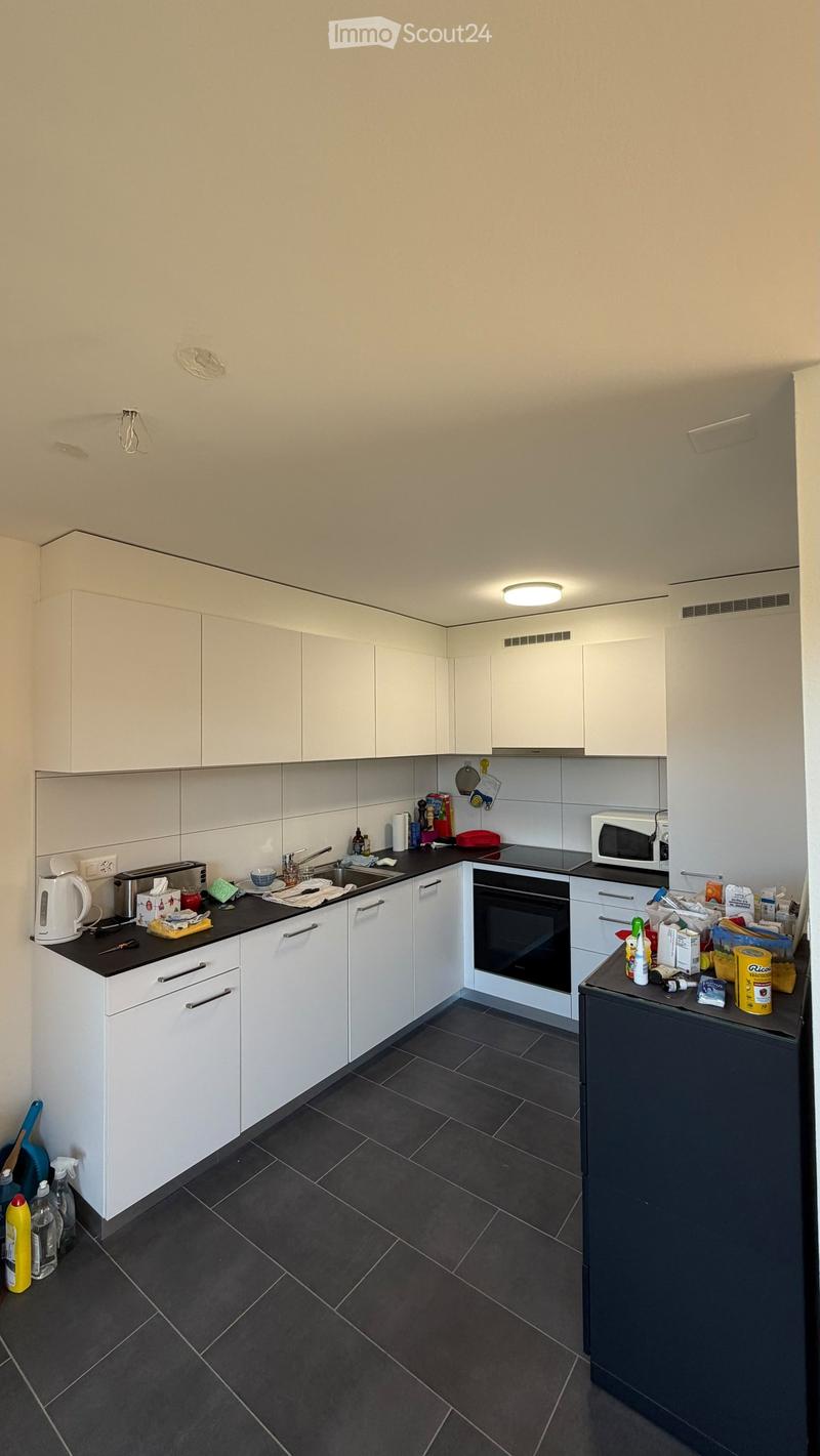 Modern kitchen with white cabinets, black countertops, and dark tiled flooring. Appliances include an oven, microwave, and toaster. Various kitchen items are placed on the countertops.