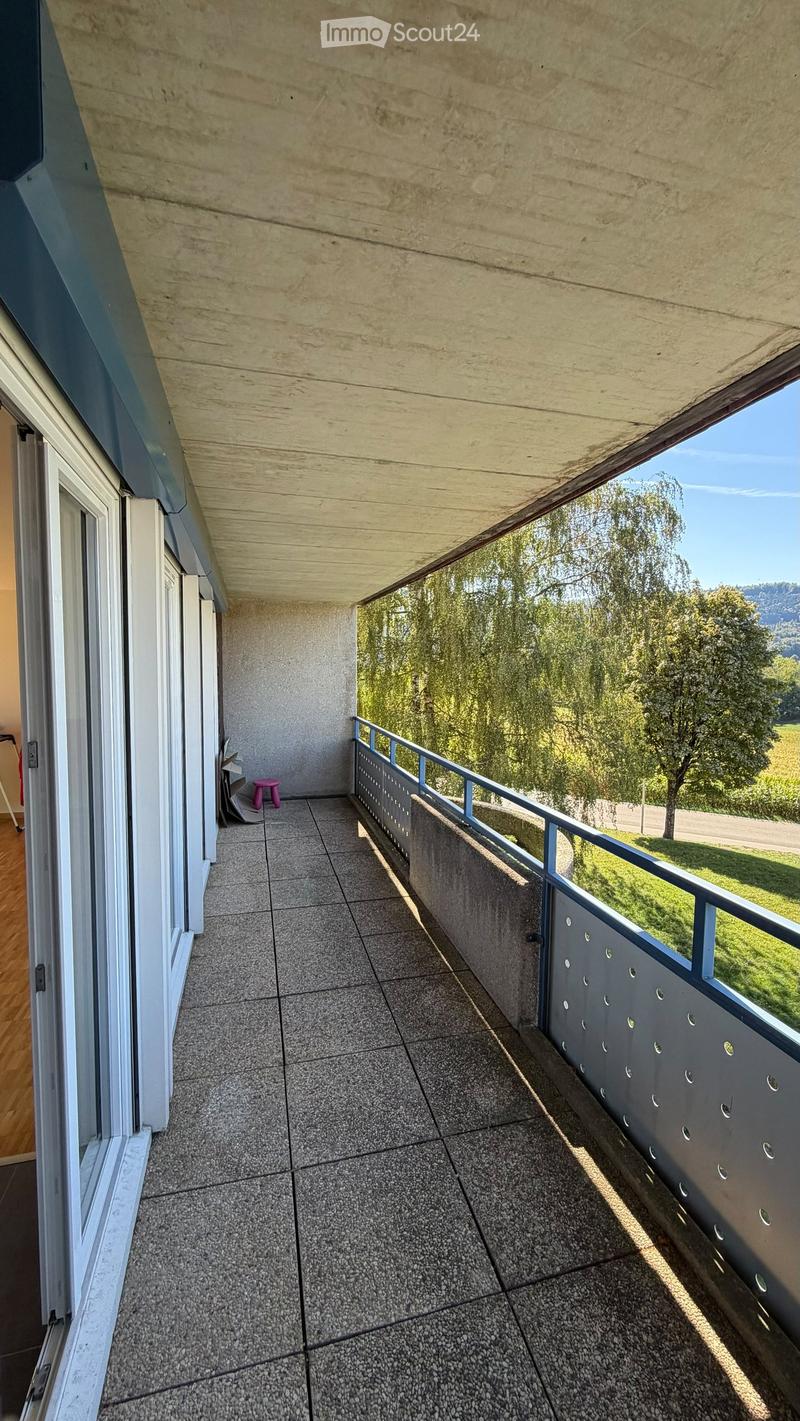 Balcony with tiled floor, metal railing, and a view of greenery and trees.