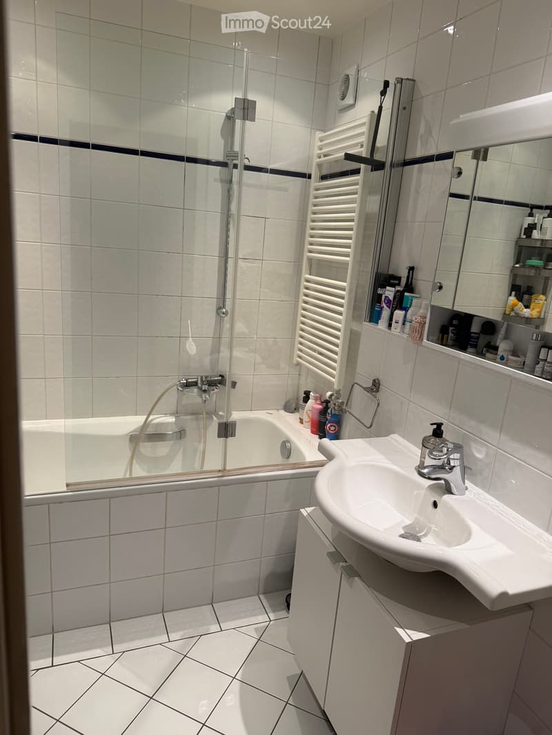 Modern bathroom with white tiles, bathtub, sink, mirror, and towel rack.
