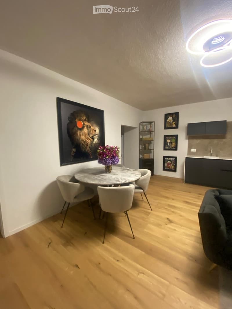 Modern dining area with a round marble table, four chairs, a sofa, a shelf, and framed artwork on the walls.