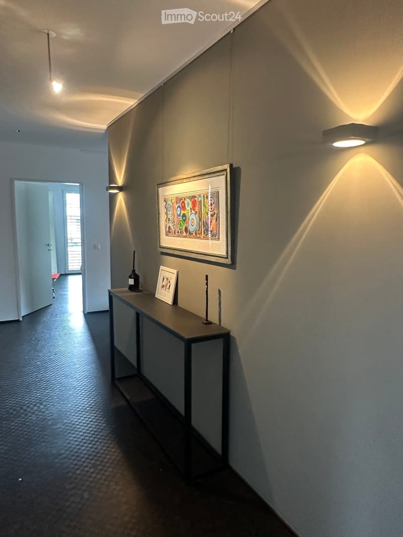 Hallway with dark flooring, a small table with decorative items, and artwork on the walls.