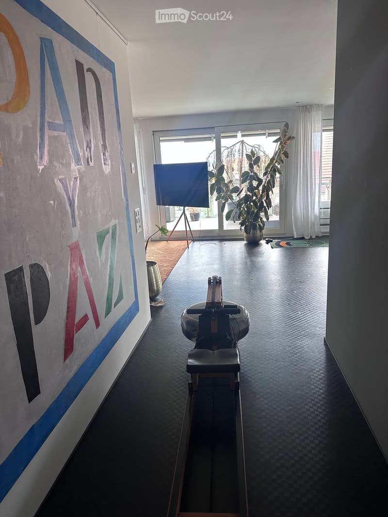 A modern hallway with a dark checkered floor, large wall art, a treadmill, and a potted plant near a glass door leading outside.
