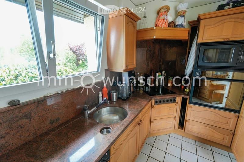 The kitchen features wooden cabinets, a granite countertop, a stainless steel sink, and various appliances including a microwave and oven. The space is well-lit with natural light from a large window.