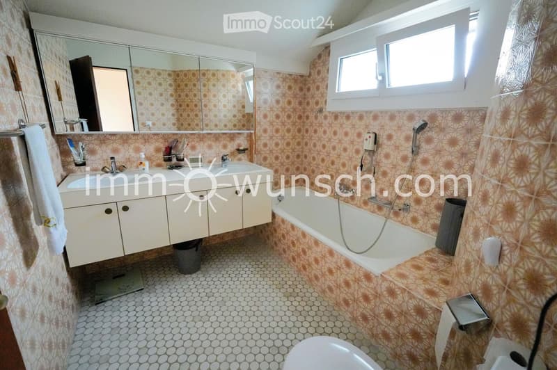 Bathroom with a double sink, bathtub, mirror, and tiled walls and floor. Includes a towel, toilet, and showerhead.