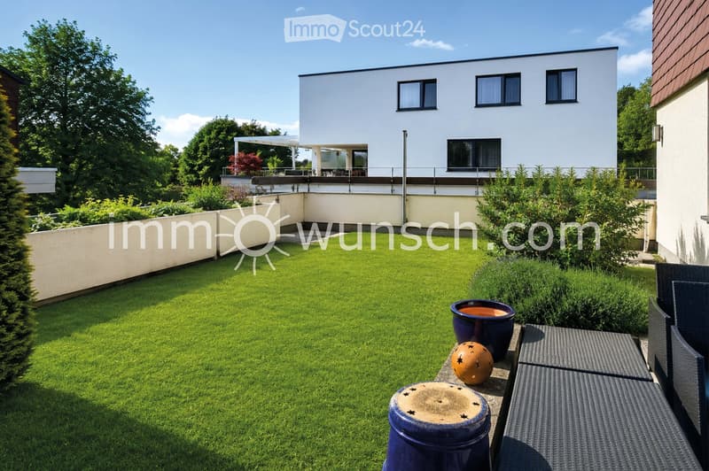 Well-maintained garden with green lawn, patio seating area, and decorative pots.