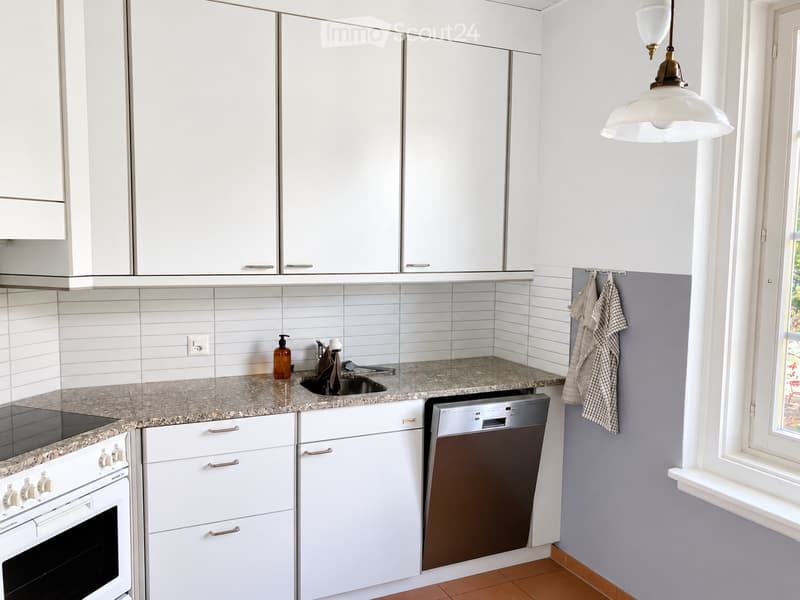 Modern kitchen with white cabinets, granite countertops, built-in oven, dishwasher, and pendant light fixture.