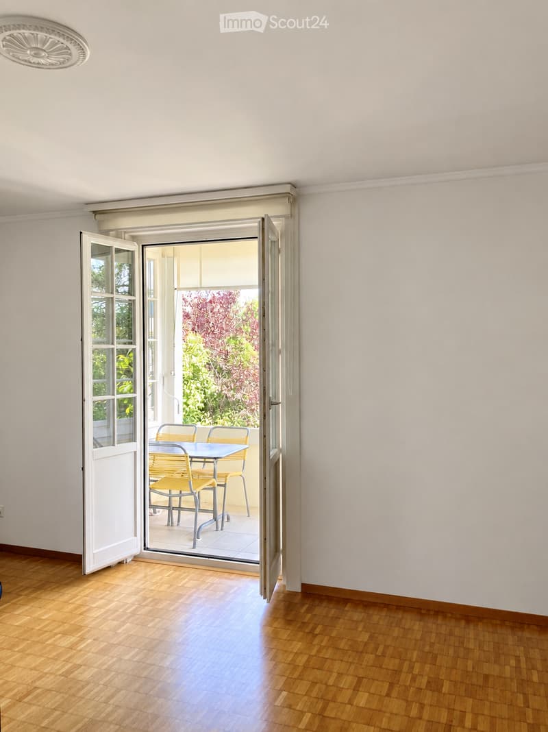 Open sliding glass doors lead to a small outdoor seating area with a table and chairs, surrounded by greenery.