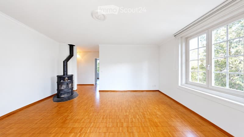 Empty room with wooden flooring, white walls, large windows, and a fireplace with a chimney.