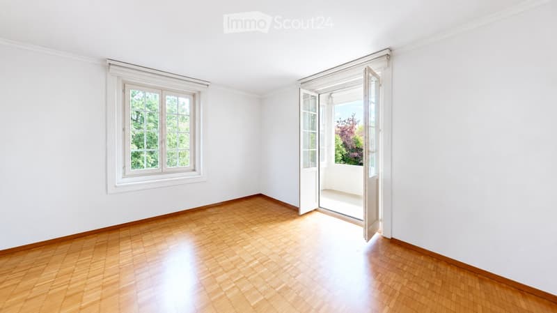 Empty room with white walls, wooden floor, large window, and open door leading to a balcony or terrace.