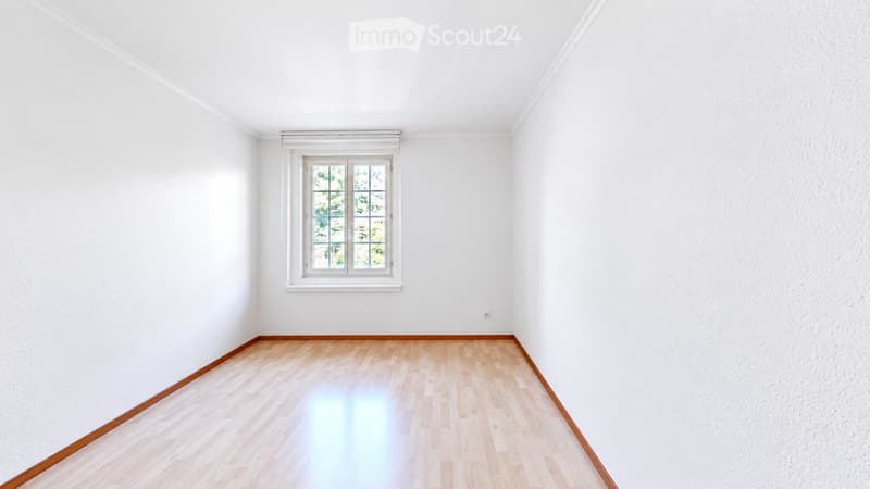 Empty room with white walls, wooden floor, and a single window with white frame.