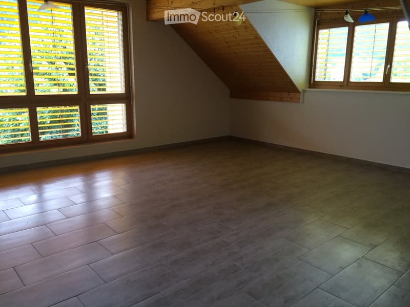 Empty room with wooden flooring and large windows with yellow blinds, featuring a sloped wooden ceiling and natural light.