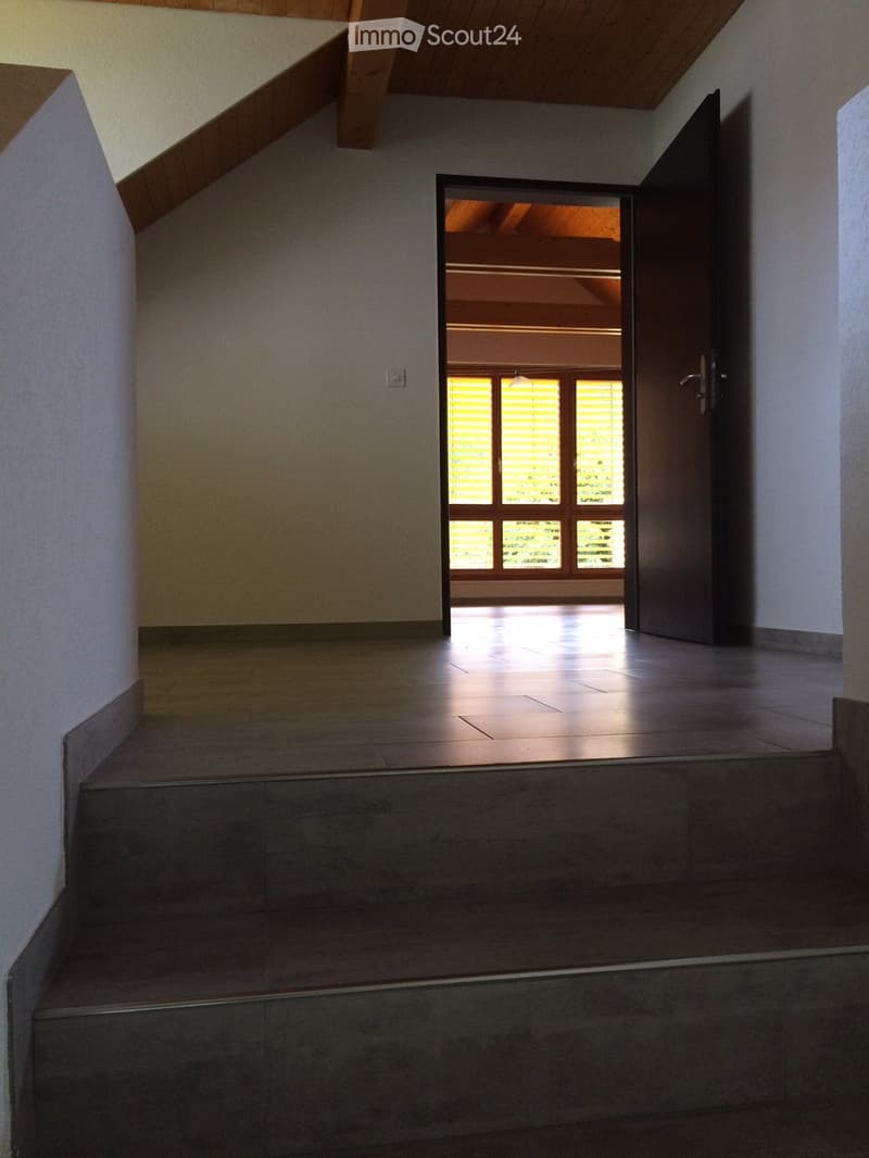 Empty hallway with wooden ceiling, tiled floor, and an open doorway leading to a brightly lit room with large windows and blinds.