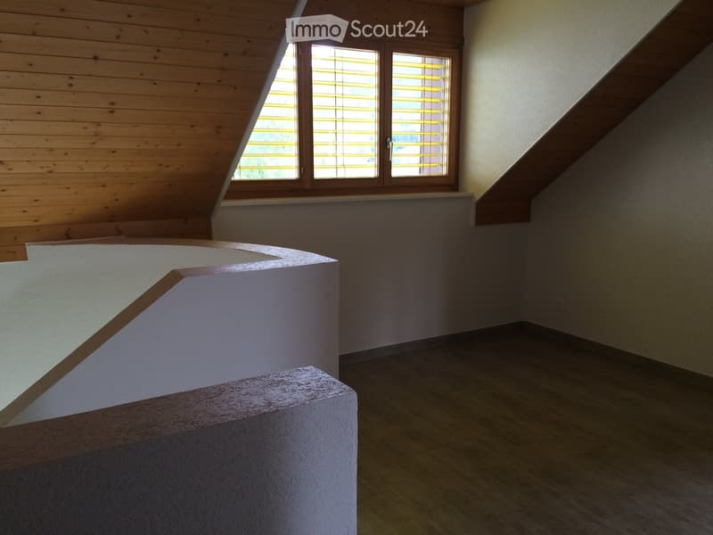 Empty room with wooden walls, slanted ceiling, large window with blinds, and a white countertop structure.