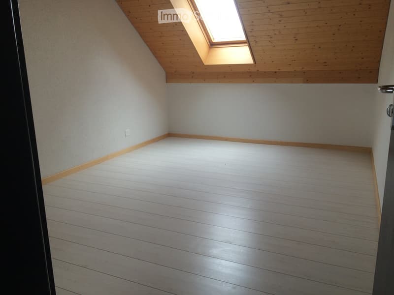 Empty room with wooden flooring, white walls, and a skylight window in the slanted wooden ceiling.