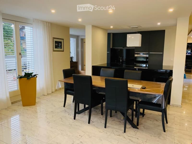 large dining table with black chairs, marble flooring, kitchen with modern cabinets, black countertop, yellow potted plant, white curtains, picture frame on the wall