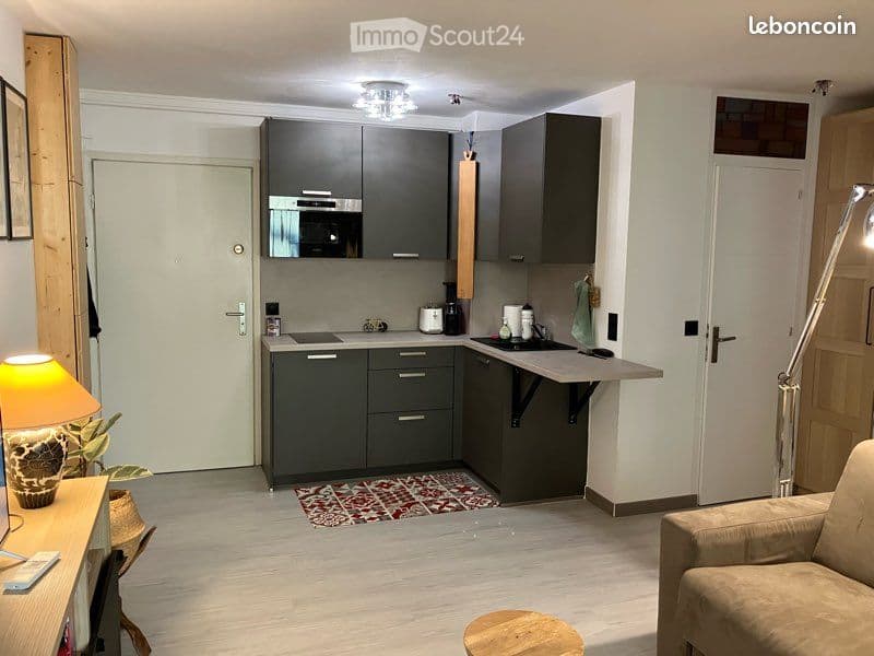 {"visible_features": [], "type": "Room", "description": "compact kitchen with gray cabinets, wooden countertop, microwave, coffee maker, sink, rug, bright lighting, white walls, beige sofa, small desk, lamp, potted plant"}