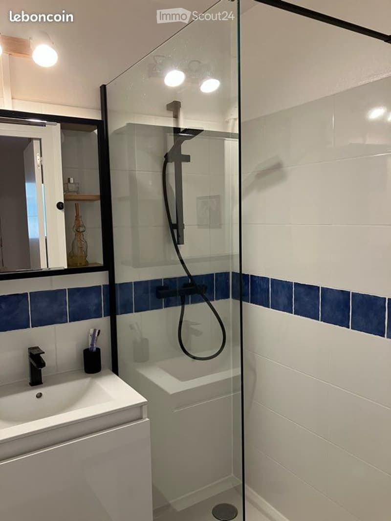 white and blue tiles, glass shower enclosure, white sink, mirror, built-in shelves