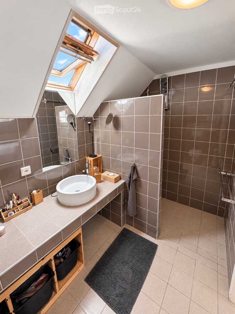 Modern bathroom with a skylight window, a white sink, a wooden shelf, a towel, and a black bathroom rug.