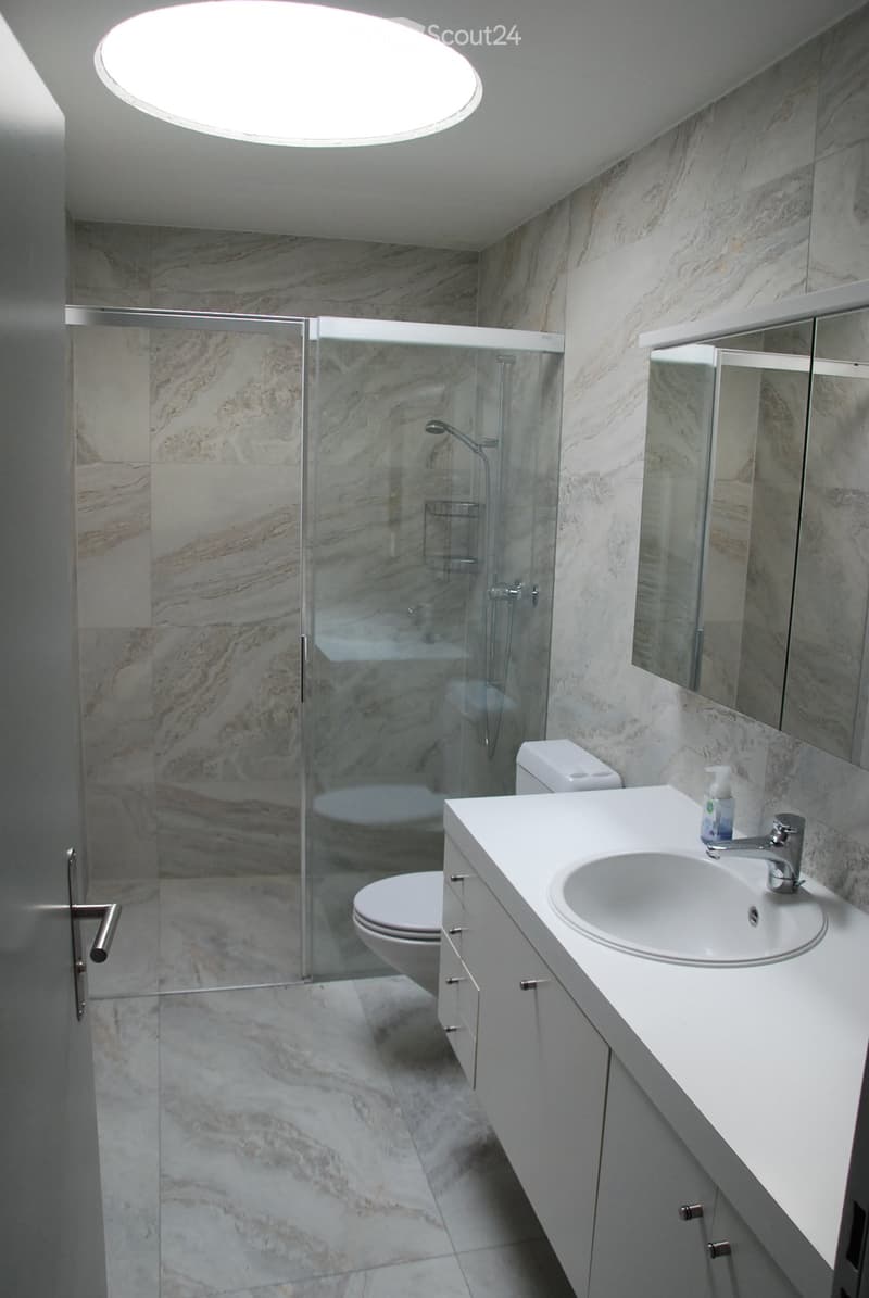 Modern bathroom with marble tiles, a glass-enclosed shower, a white sink with a modern faucet, and a toilet.