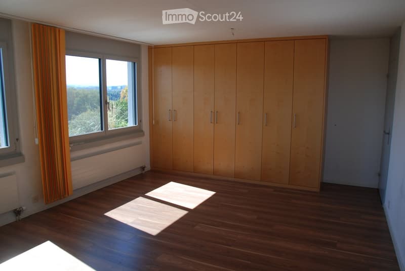 Empty room with wooden flooring, large built-in wardrobes, and large windows with striped curtains. Natural light streams in, illuminating the space.