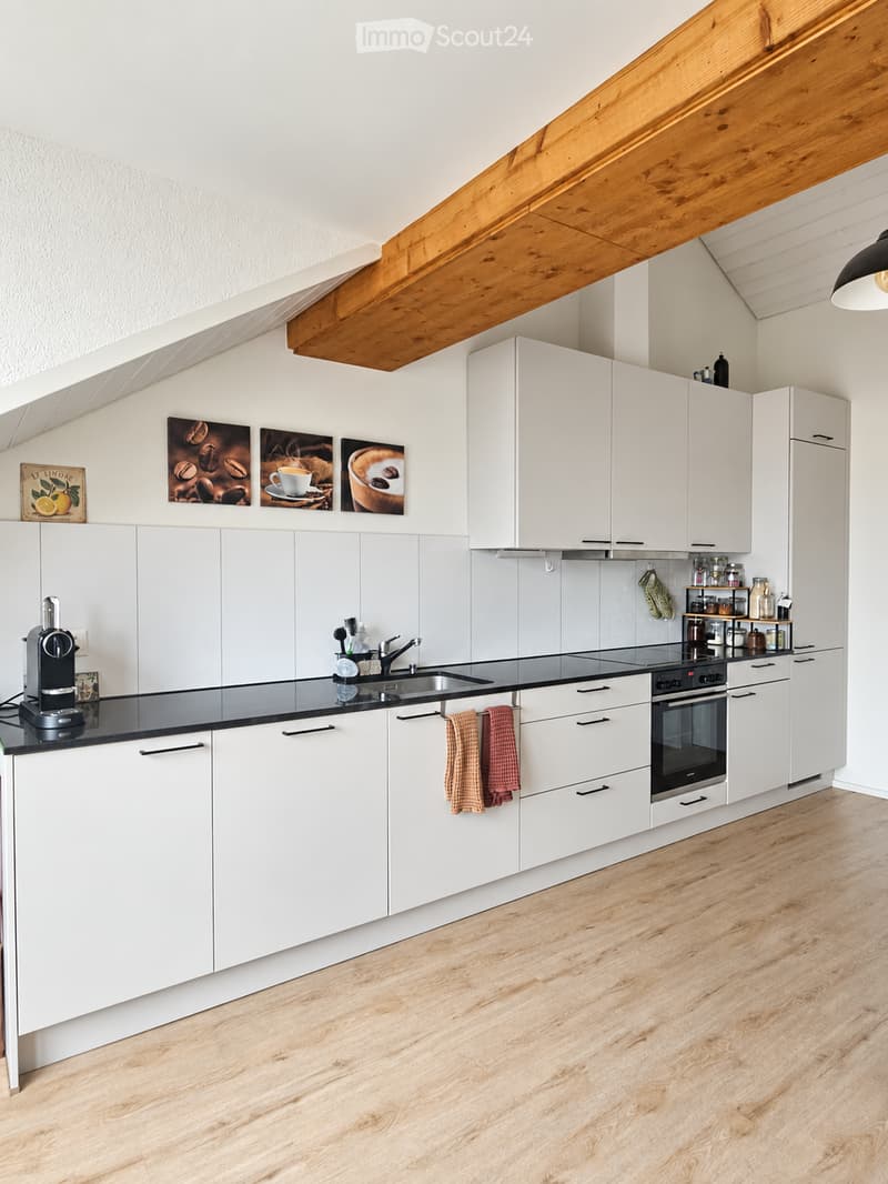 Modern kitchen with white cabinets, black countertops, and wooden flooring. Features a sink, coffee machine, and decorative picture frames.