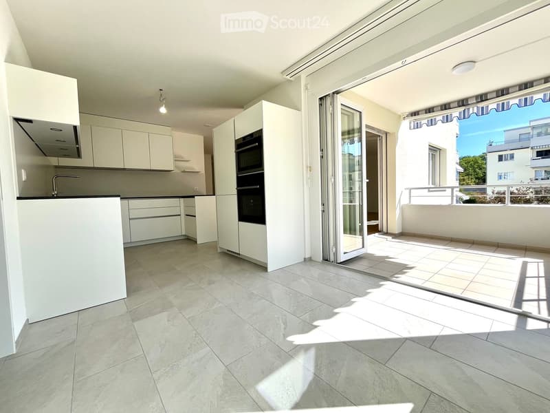 Modern kitchen with white cabinets, an oven, and a faucet, opening onto a tiled balcony with a view of the city.