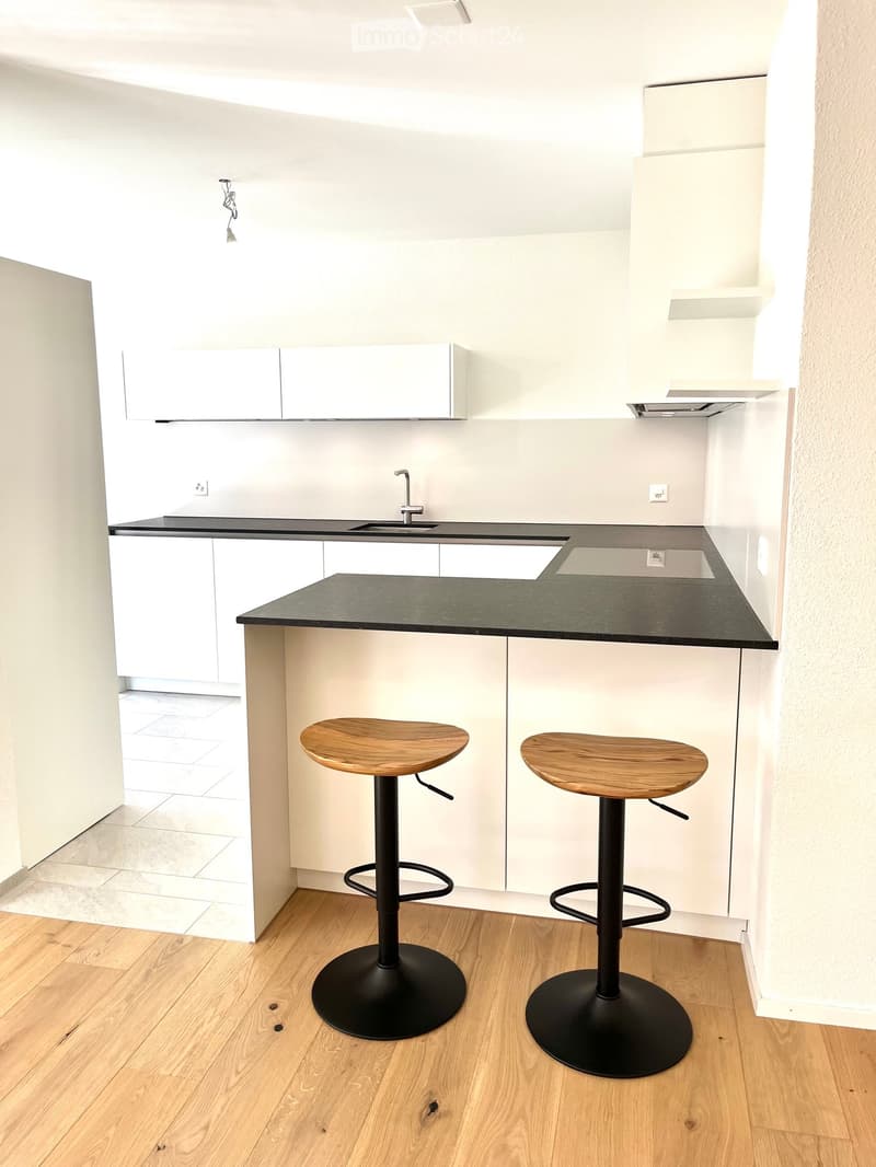 Modern kitchen with white cabinets, black countertop, and two wooden stools at the island.