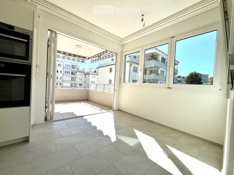Bright balcony with tiled flooring, large windows, and an open sliding door leading to an outdoor area.