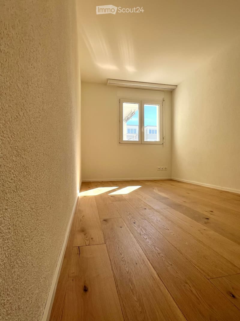 Empty hallway with wooden flooring, light-colored walls, and a window at the end.