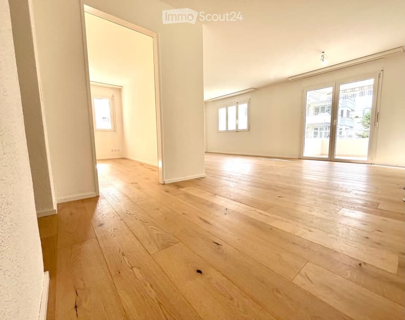 Empty room with light wooden flooring, white walls, large sliding glass doors leading to a balcony, and a window on the opposite wall.