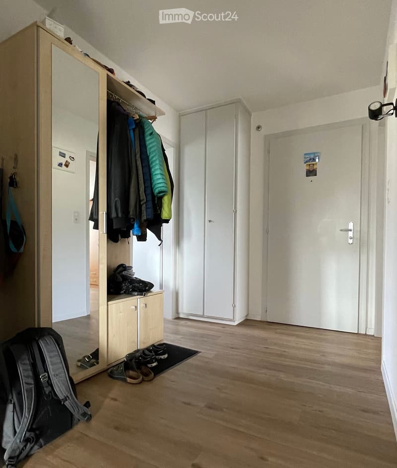 Entrance hallway with wooden floor, clothing storage unit with mirror, shoe rack, backpack, and door.