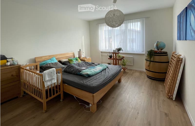 Bedroom with bed, crib, wooden dresser, small shelf with plants and decorative items, and a chandelier