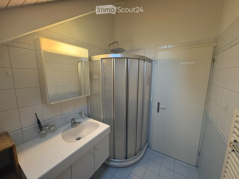 Modern bathroom with a white sink, mirror with built-in lighting, a round glass shower enclosure, and a radiator. The walls are tiled with a decorative border near the ceiling.