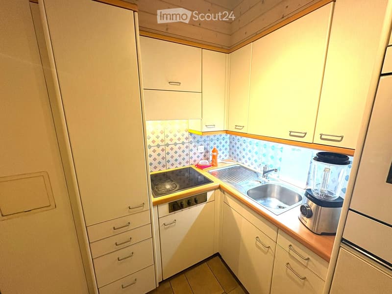 Compact kitchen with white cabinets, a sink, a stove, and a blender on the counter.