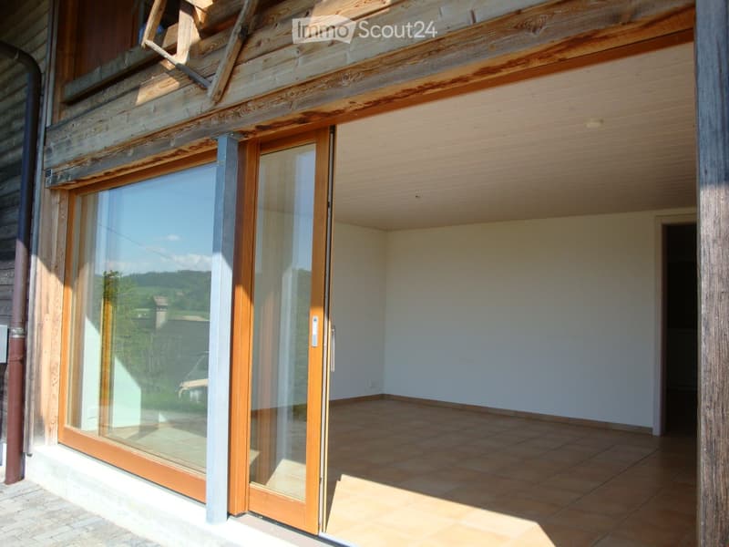 Empty room with tiled floor, white walls, and large sliding glass doors opening to a wooden deck with a scenic view.
