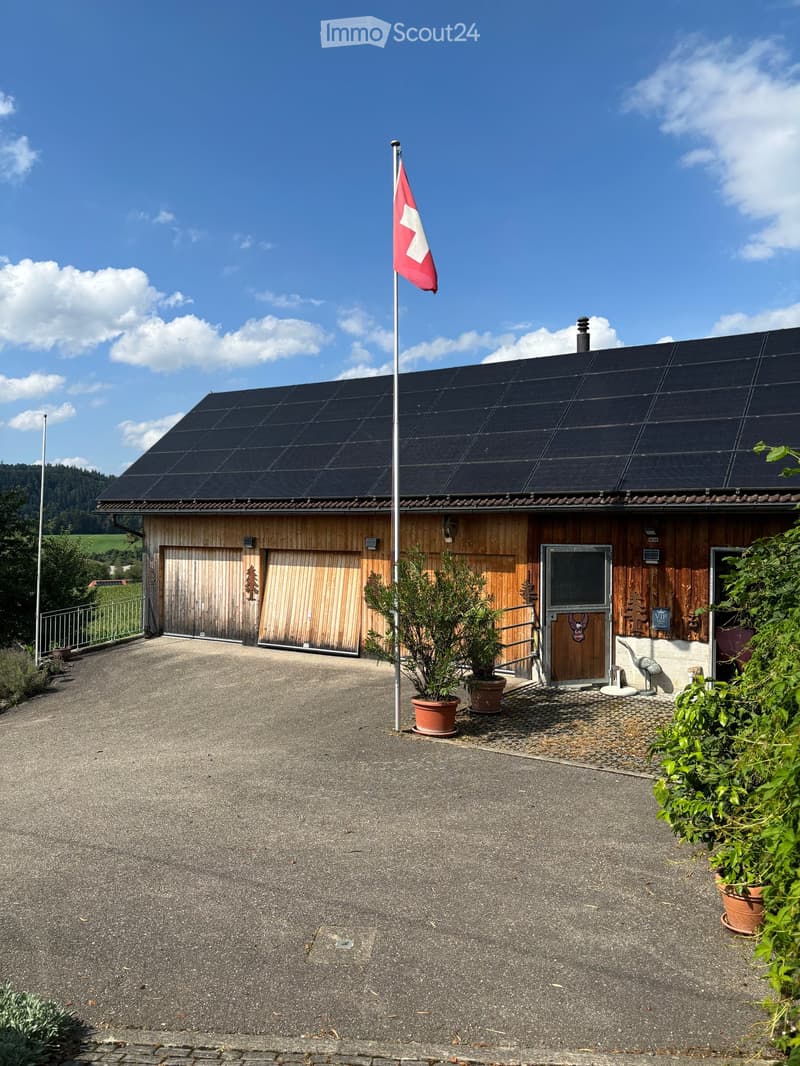 A modern wooden building with solar panels on the roof, a Swiss flag, and a garage entrance.