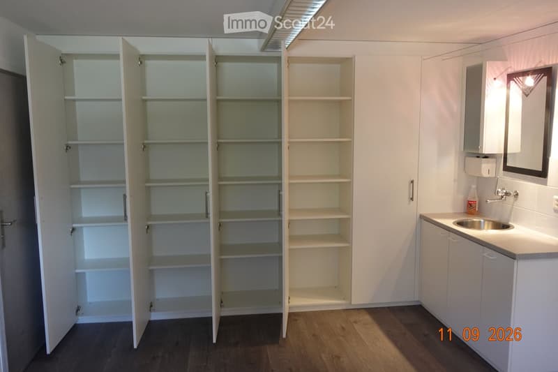 Empty room with white built-in cabinets and shelves, a sink, and a mirror on the wall. The floor is wooden.
