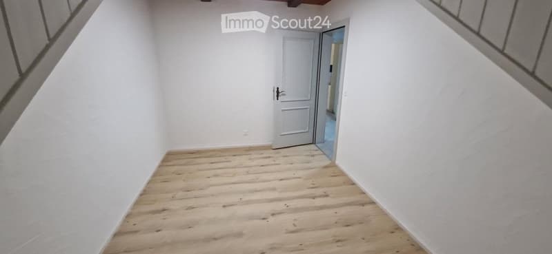 Empty room with wooden flooring and white walls, featuring a single door leading to another space.