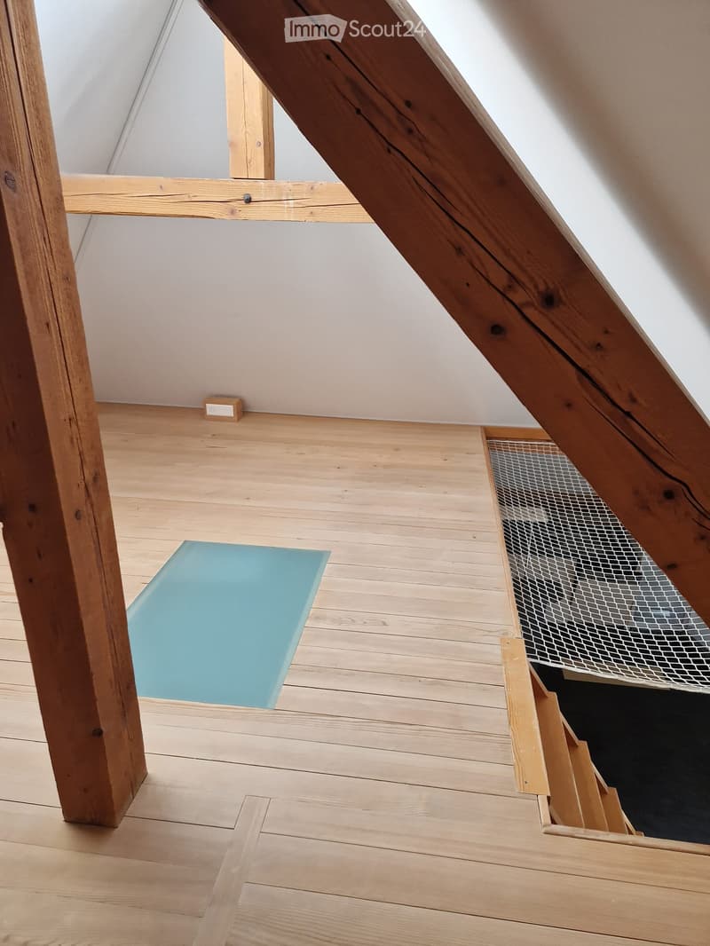 an attic with wooden floor, blue yoga mat, exposed wooden beams, white wall