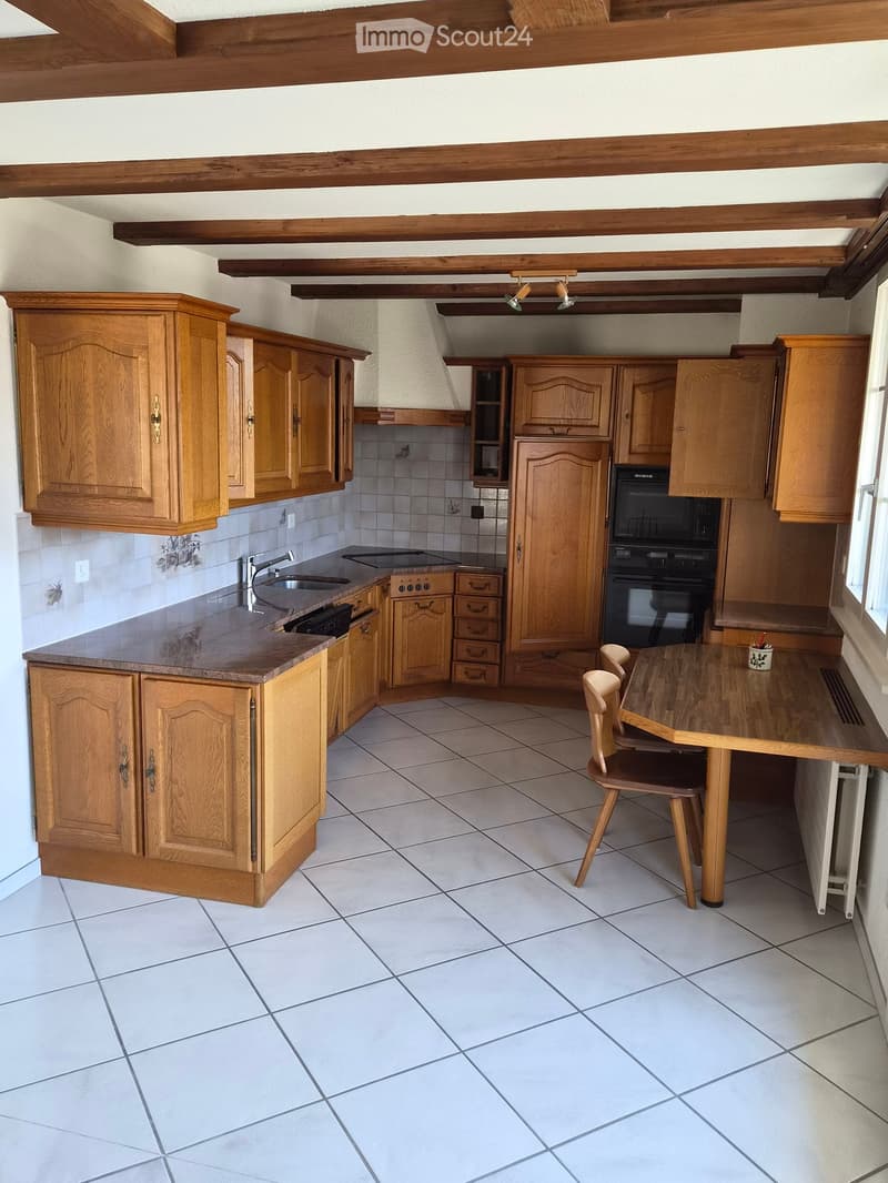 A well-lit kitchen with wooden cabinets, a central island, a sink, stove, oven, and a small dining area with a table and chairs.