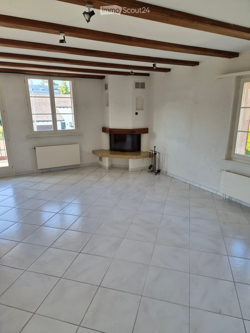 Empty room with tiled floor, exposed wooden beams on the ceiling, fireplace, radiators, and windows.