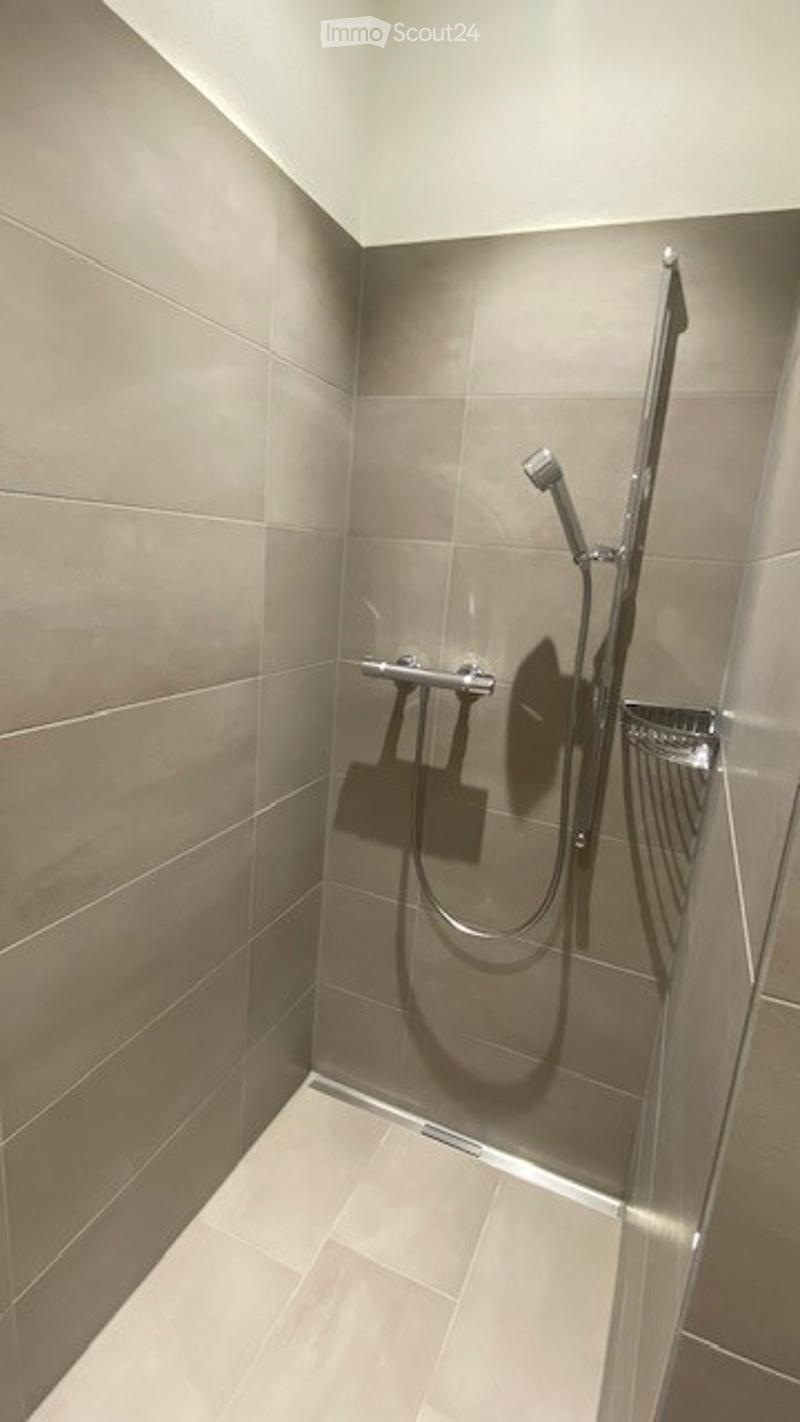 Modern shower area with grey tiles, a handheld showerhead, and a built-in shelf.