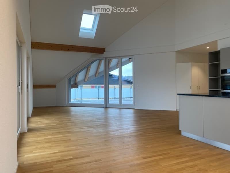 Bright, open loft-style room with wooden flooring, large windows, and a skylight. Minimalist design with white walls and exposed wooden beams.