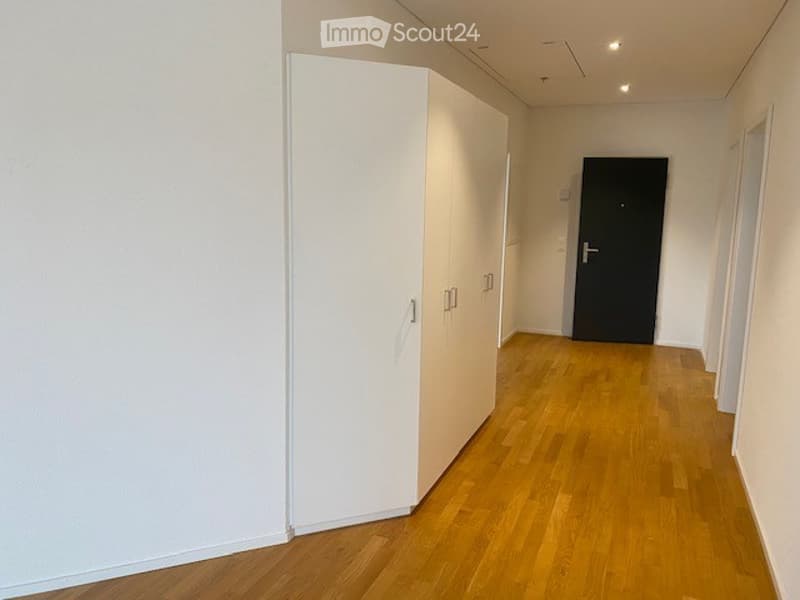Empty hallway with wooden flooring, white walls, and a closed black door at the end.