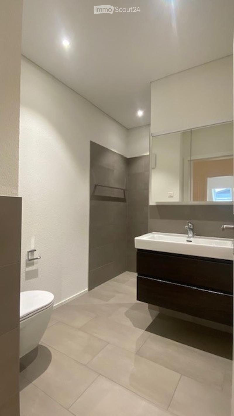Modern bathroom with white tiled floor, dark wooden cabinet, white sink, toilet, and large mirror above the sink.